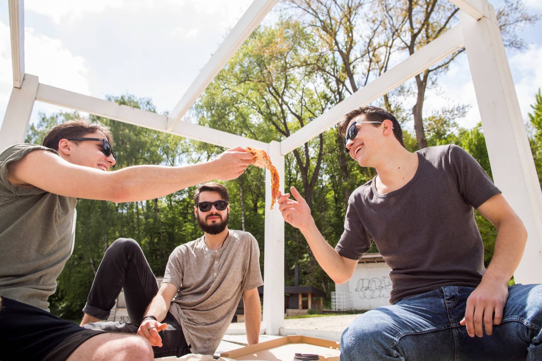 Friends sharing pizza under a wooden pavilion
